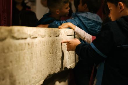 Niño tocando una inscripción romana de la exposición Tresors de la Vila Joiosa